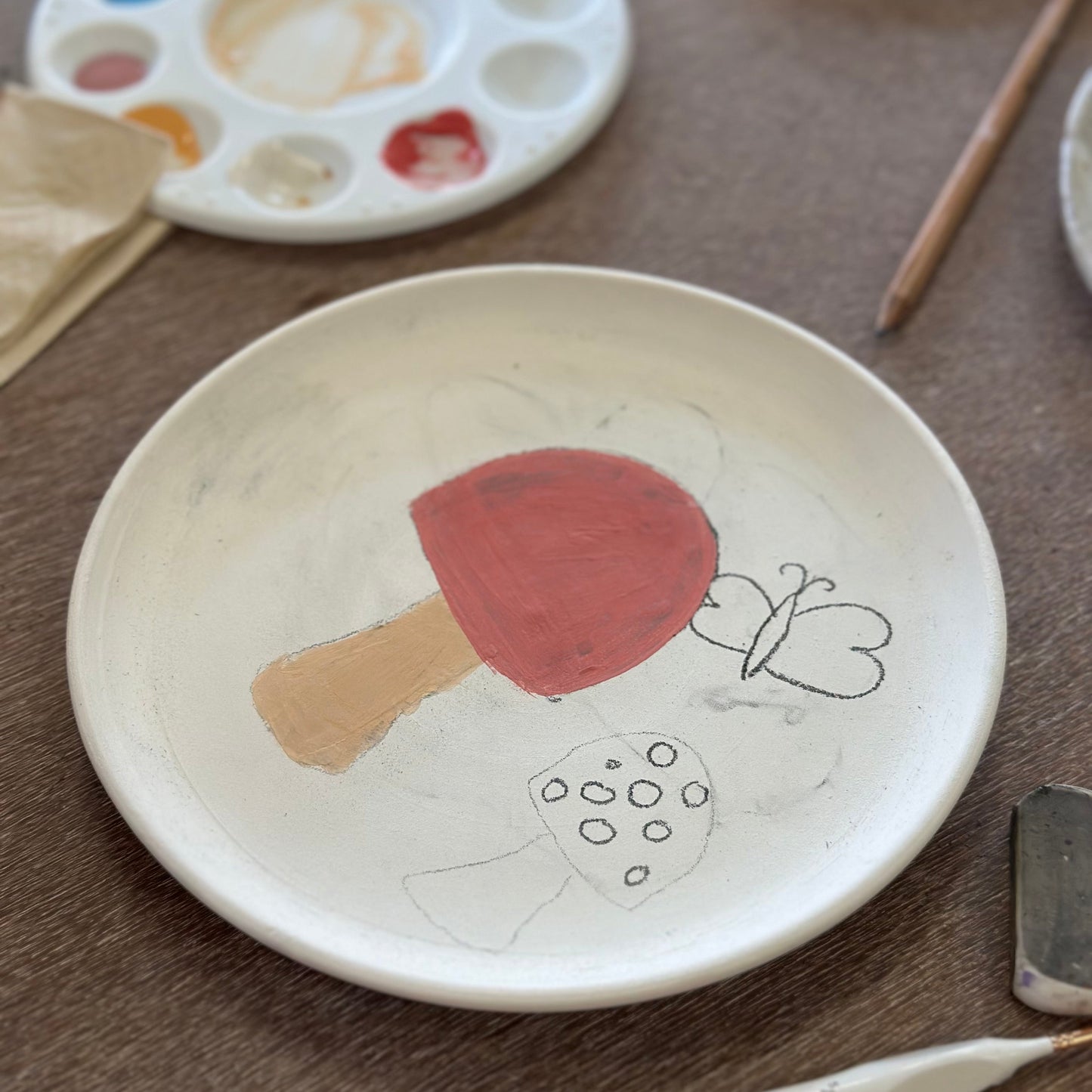 Ceramic plate with a ladybug design on a wooden surface with painting tools.